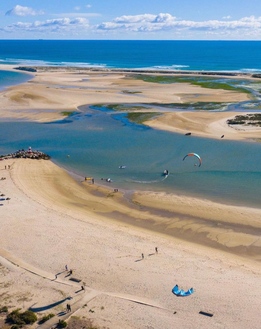 Plage dorée au Portugal vue d’en haut avec dunes et baïne, horizon bleu et activités nautiques sur l’eau. location villa de luxe portugal.