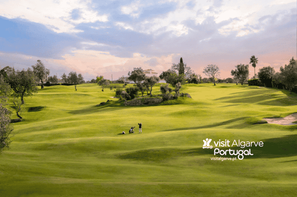 Lush green golf course at sunset with trees, players on the fairway, and “visit Algarve Portugal” watermark.