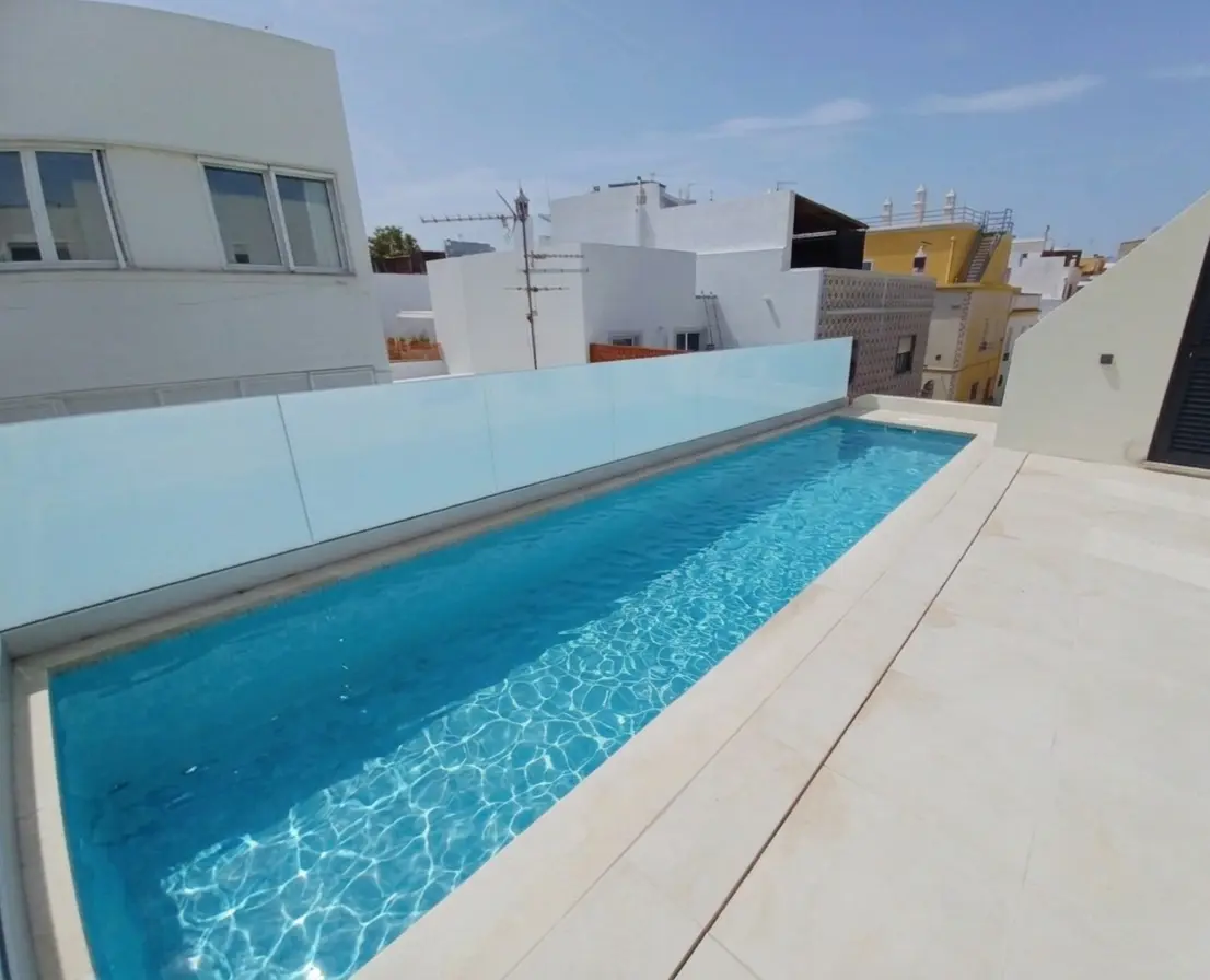 Piscine rectangulaire sur terrasse d'une maison de charme, espace lumineux et modernisé, vue sur bâtiments blancs du village.