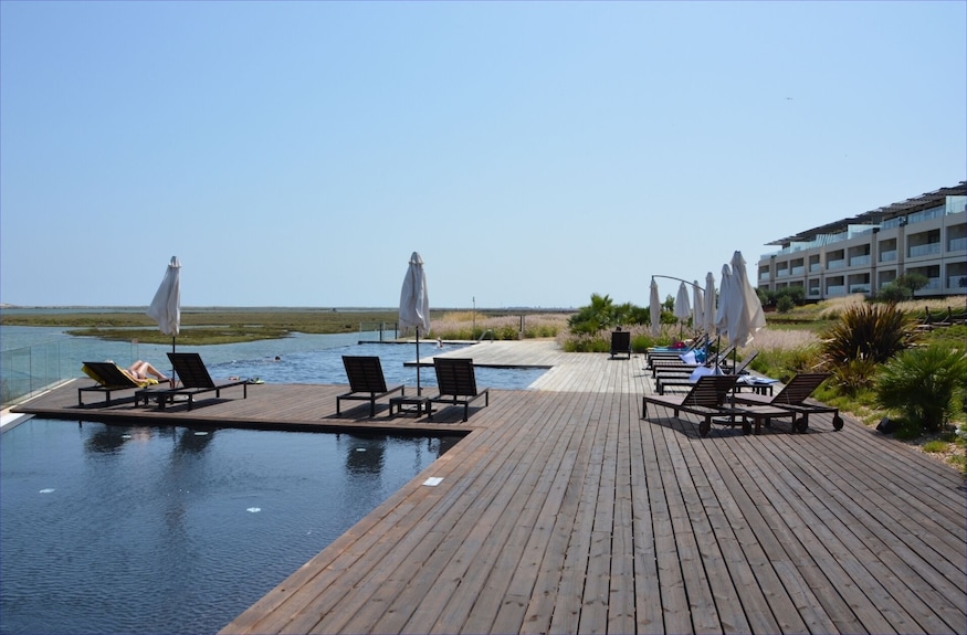 Sunloungers on a wooden pool deck by the sea with a lagoon, Fuseta villa resort backdrop (villa rentals fuseta)