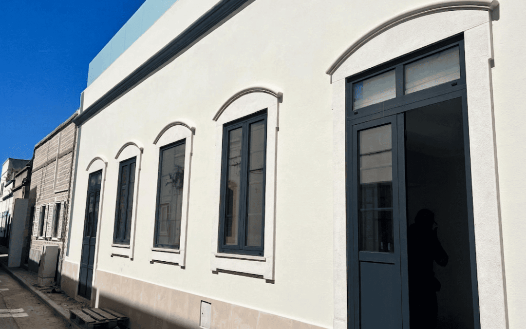 Villa de charme ria formosa: façade blanche lumineuse avec arches et fenêtres noires, porte-fenêtre bleu sombre sur une rue calme.