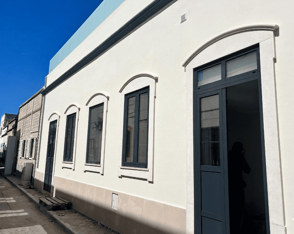 Villa de charme ria formosa: façade blanche lumineuse avec arches et fenêtres noires, porte-fenêtre bleu sombre sur une rue calme.