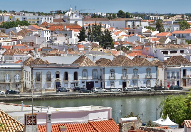 Colourful Tavira rooftops along the eastern Algarve coast, with river and whitewashed buildings reflecting in the water.