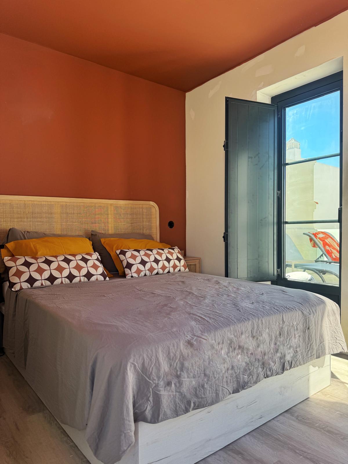 Chambre lumineuse dans une maison de prestige Algarve est avec lit double, paroi orange et fenêtre ouvrante donnant sur l’extérieur.