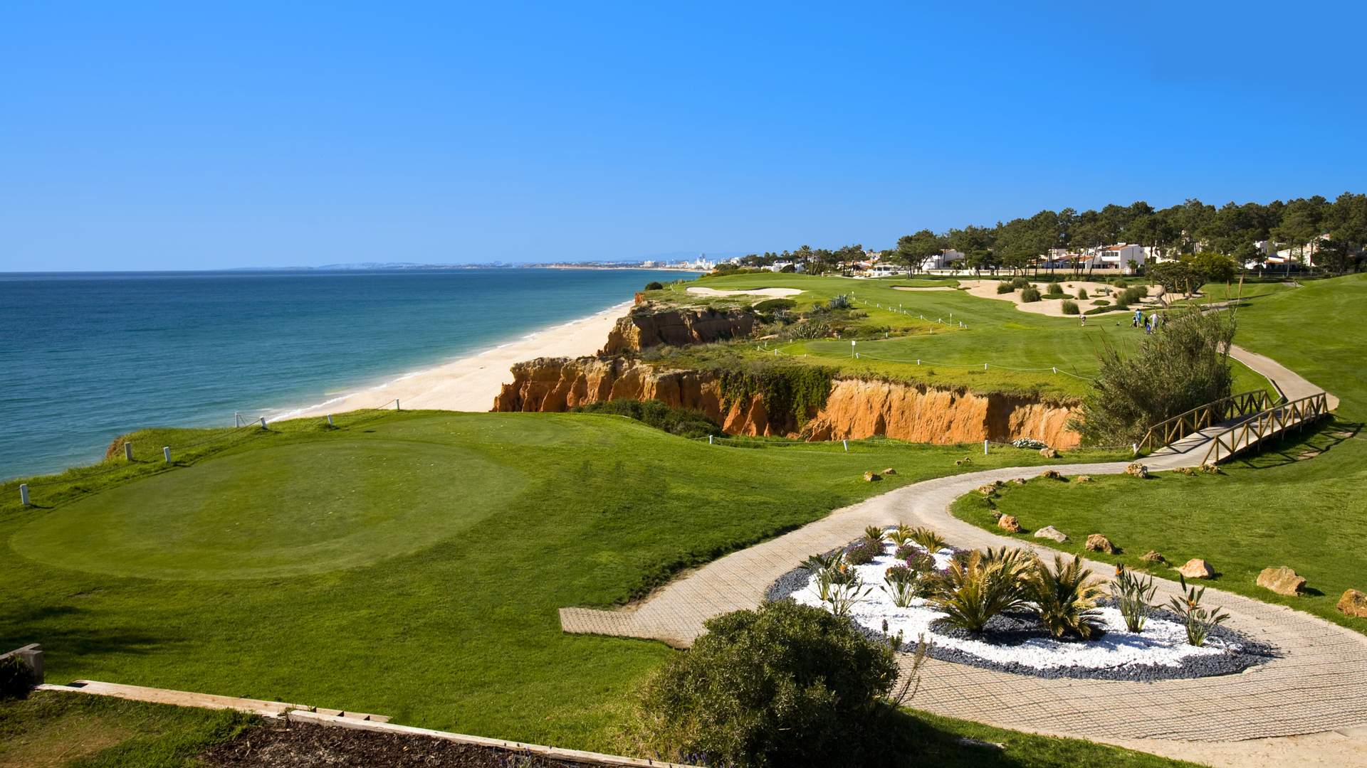 Course côtière en Algarve avec falaises et plage, parcours de golf verdoyant et chemin piétonnier menant à la mer. Hôtel Algarve demi-pension.