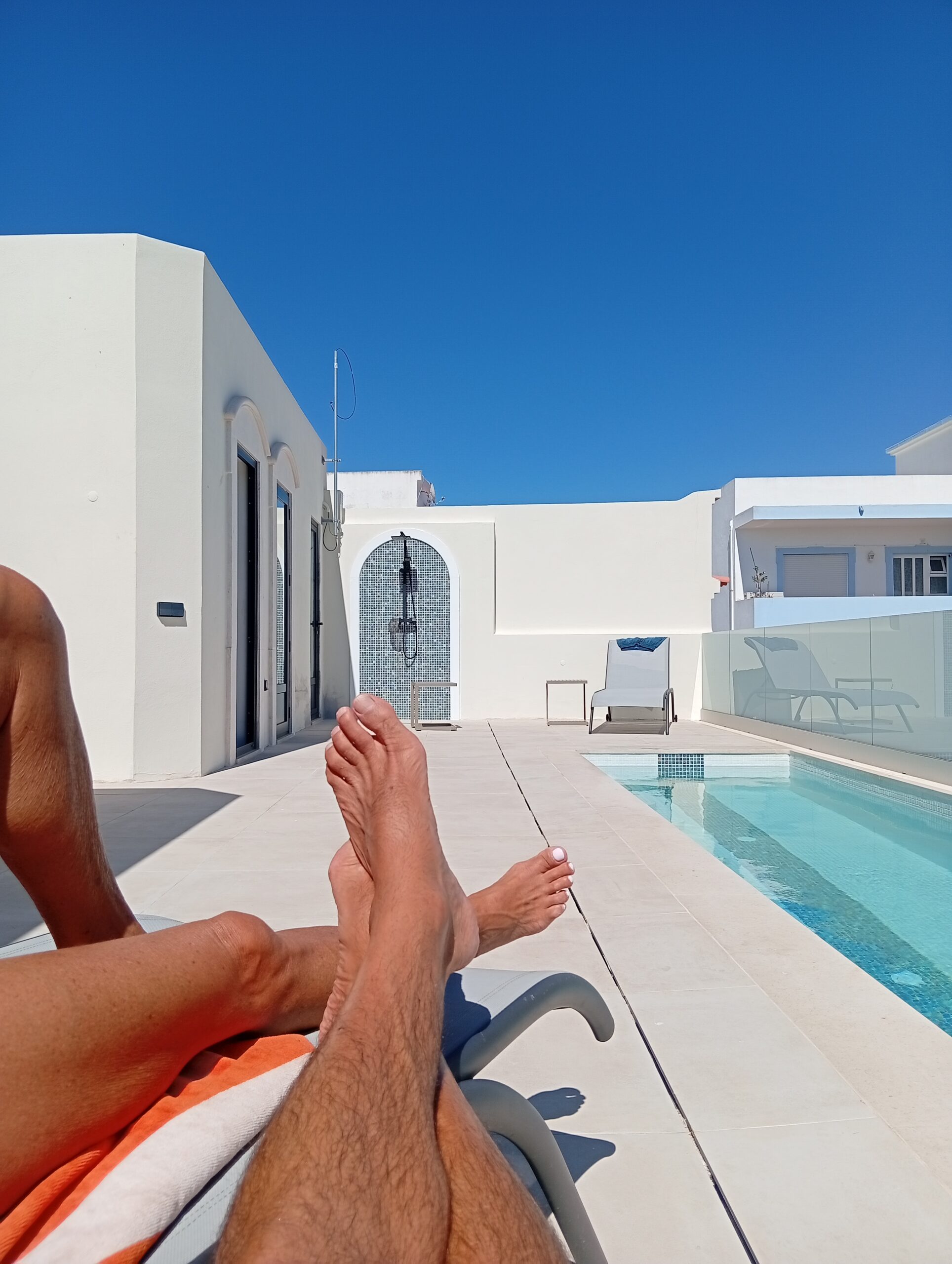 Personne se prélassant au bord d'une piscine dans une villa blanche, ciel bleu immense et terrasse lumineuse. Maison de prestige Algarve est.