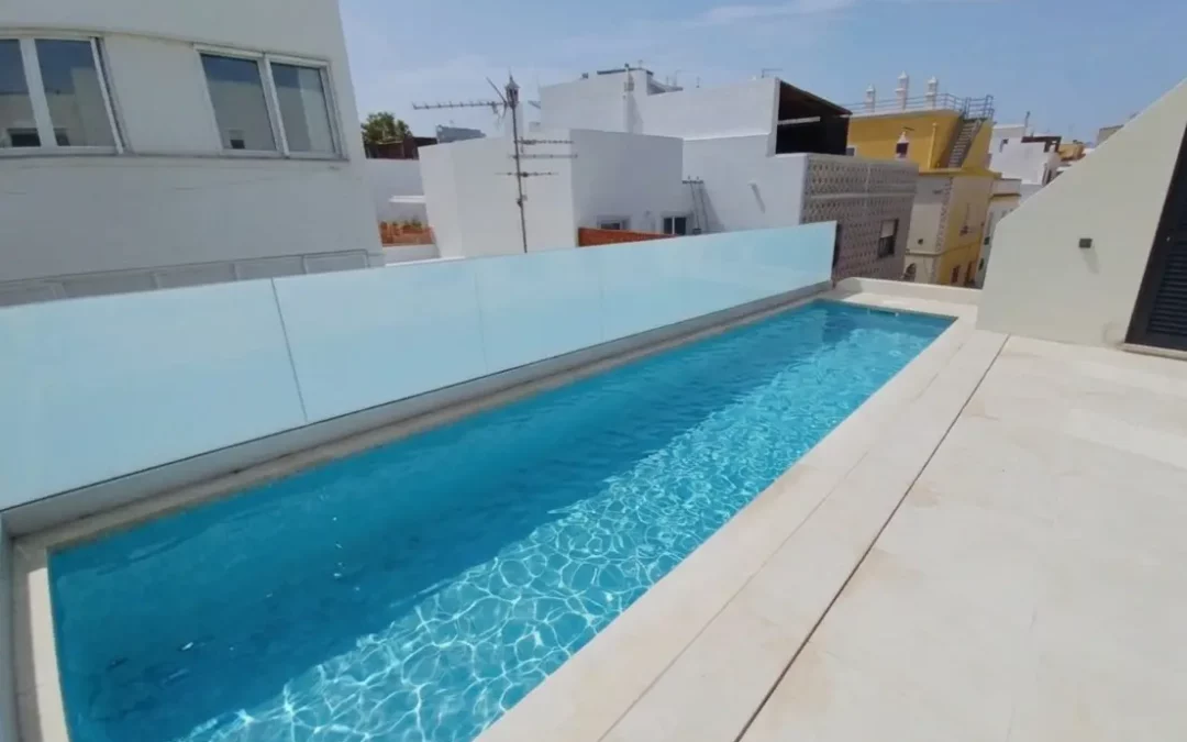 Luxurious rooftop swimming pool on a modern villa terrace, with clear blue water and surrounding white buildings under a sunny sky. Luxury rental with rooftop swimming pool portugal.